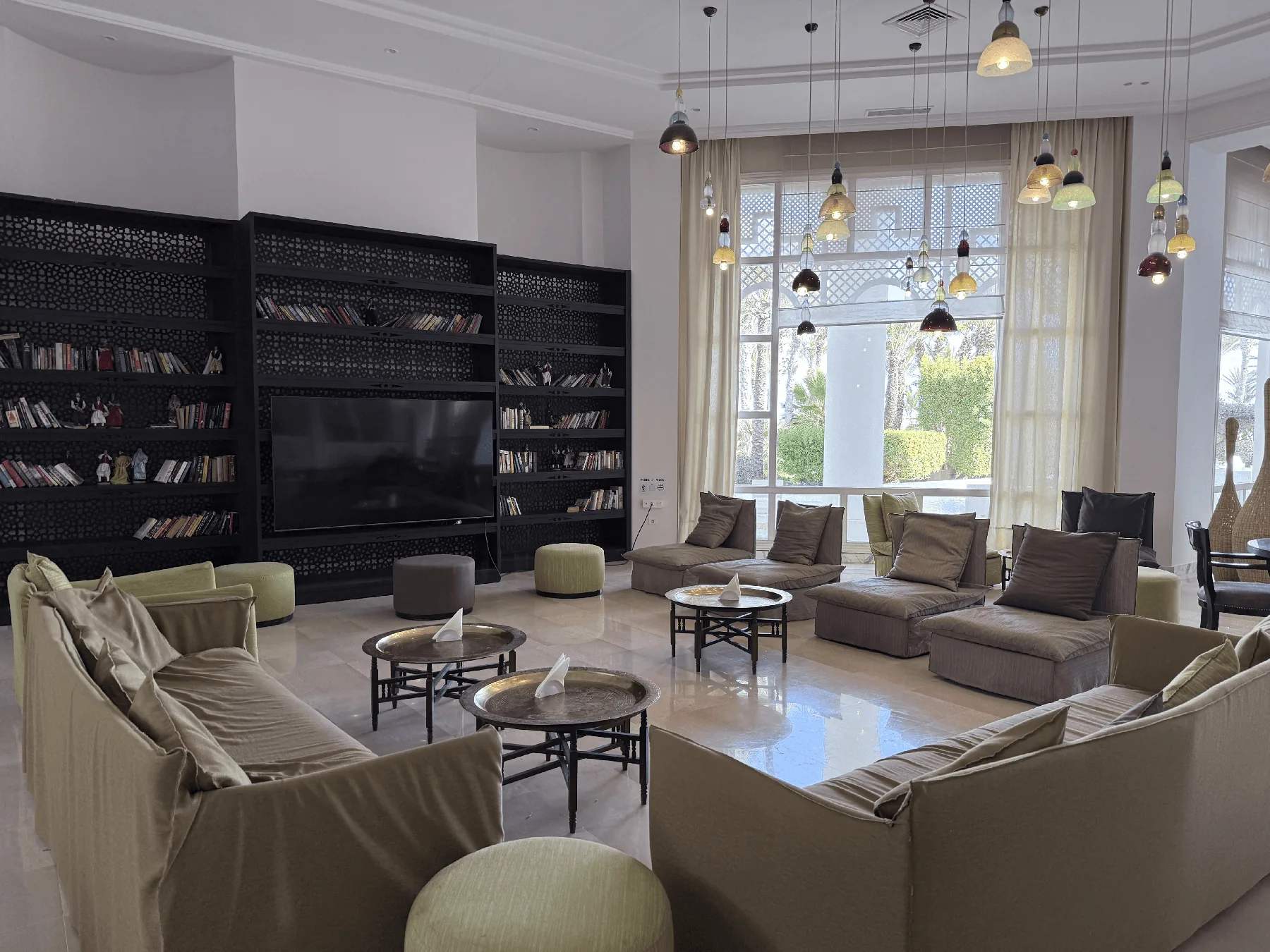 A warmly lit lounge with a wall of bookshelves, sofas, and armchairs arranged for reading and conversation