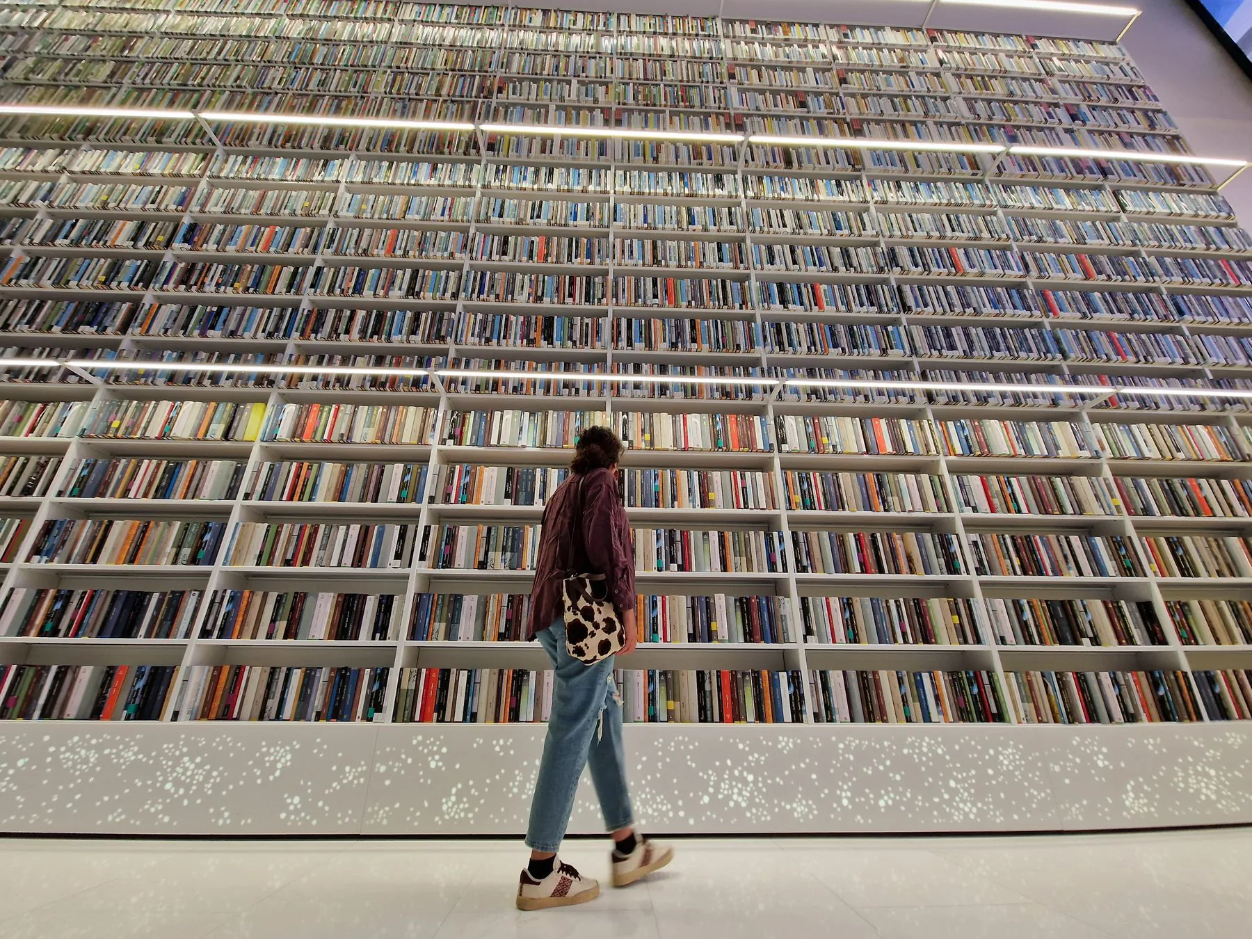A visitor browsing a towering wall-to-ceiling library shelf