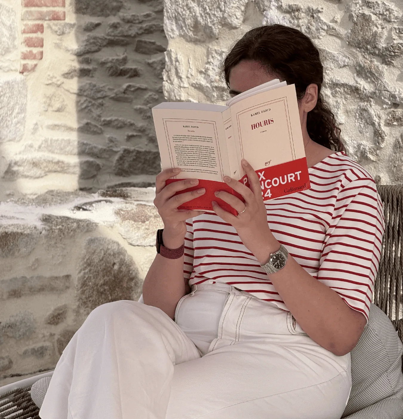 A woman reading a book against a stone wall