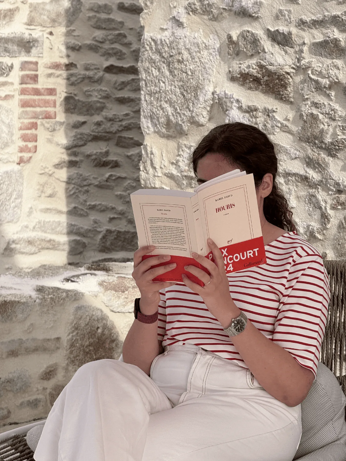 امرأة تقرأ كتابًا أمام جدار حجري
